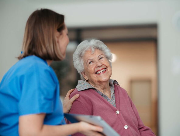 Eine Pflegekraft lächelt mit einer Seniorin, Teil des Pflegenetzwerks in Börde, und bietet Unterstützung an.